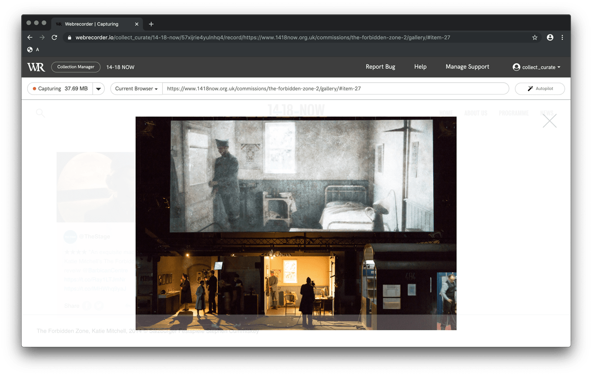 Screenshot of an archived webpage featuring a wide angle photograph of a theatre stage set by Stephen Cummiskey. Above the stage, is a large projected image of a soldier in uniform standing inside the doorway of a small bedroom. The colours are cool greens, and pale greys. Upon the stage itself, are two interiors, lit with warm golden light. The stage rigging and lighting are visible in the shadows.